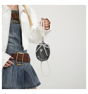 Détail d'un mini sac en denim noir avec nœud en dentelle et bandoulière en perles