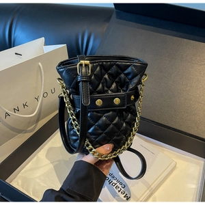 Detailed view of black quilted bucket bag with gold chain and studded leather strap