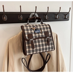 Detail of vintage plaid backpack featuring dog embroidery on wood hook background