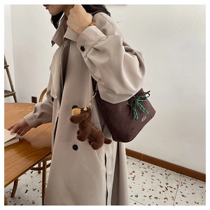 Detail of a brown suede bucket bag with a green bow and a plush dog charm pendant