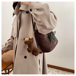 Detail of dark brown suede bucket bag with green woven drawstring and plush dog charm
