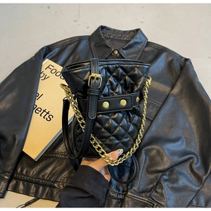 Close-up of quilted black bucket bag with gold chain and studs on leather background