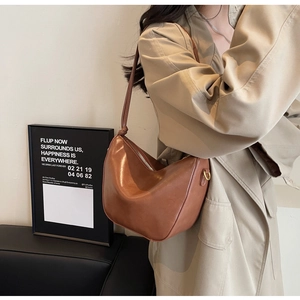 Detail of a brown vintage half-moon shoulder bag styled with a classic beige trench coat
