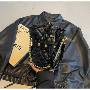 Macro shot of black quilted bucket bag with gold chain strap and buckle detail