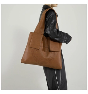 Side view of a large brown tote bag with round stitching and wide strap on model