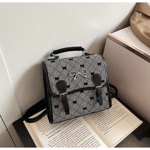 Detail of tweed flap bag with metal bow accent, black leather trim, and handle on open book