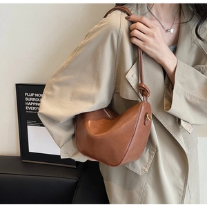 Detail of a brown leather crescent shoulder bag with a unique decorative knot on the strap