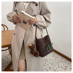 Detail of suede bucket bag featuring green plaid bow and plush dog charm pendant