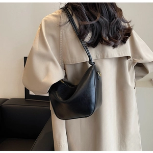 Minimalist black leather hobo bag with knotted shoulder strap shown on a beige trench coat