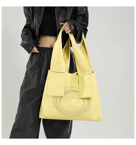 Detail of large yellow tote bag featuring modern black circular print and soft faux leather texture