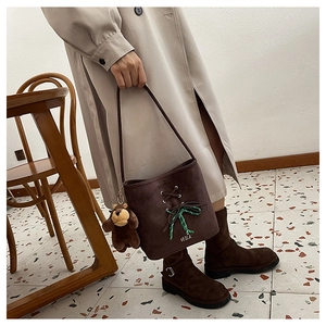 Detail of dark brown suede bucket bag featuring a plaid bow and cute bear plush charm