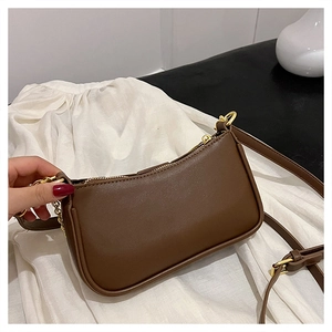Close-up of brown faux leather baguette bag with golden zipper and metal chain strap detail