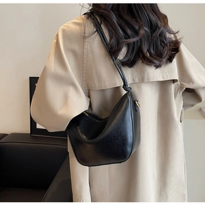 Minimalist black crescent shoulder bag in glossy leather shown on a model's back