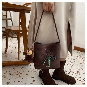Close-up of brown suede bucket bag with cross-lace design and plush bear charm detail