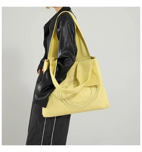 Close-up of a large yellow tote bag with black embroidered circles on a leather surface