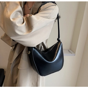 Black leather crescent bag styled with a beige trench coat for a minimalist look