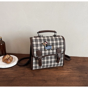 Detail of plaid tweed bag with dachshund embroidery and brown leather trim on a wooden table