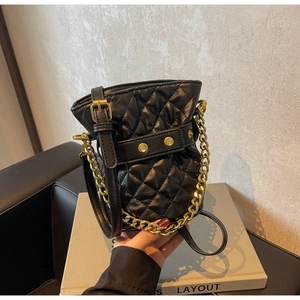 Detail of black quilted leather bucket bag with gold chain strap and drawstring closure