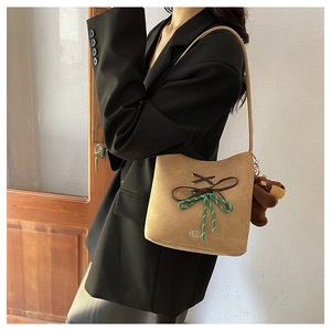 Detail of khaki suede bucket bag with woven knot, bear charm, and wide shoulder strap
