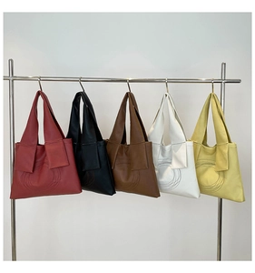Detail view of five textured faux leather tote bags in various colors on a metal hanger