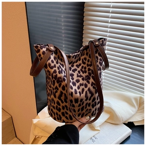 Detail showing the leopard print fabric texture and brown leather handle of the bucket bag