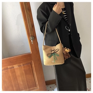 Detail of camel suede bucket bag with decorative bow and plush bear charm on side