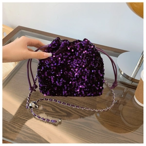 Dettaglio borsa a secchiello con paillettes viola e tracolla a catena su tavolo di vetro