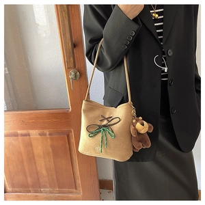 Detail of khaki faux suede bucket bag featuring a ribbon bow and plush bear charm