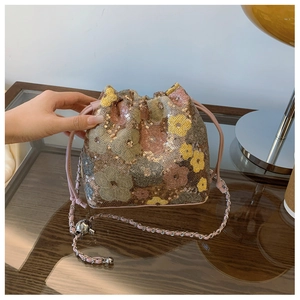 Dettaglio della borsa a secchiello con paillettes, motivi floreali rosa e tracolla a catena