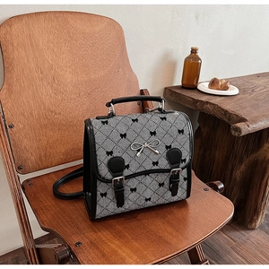 Close-up of vintage plaid backpack with black bow prints and metal buckle on a wood chair