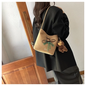 Detail of tan suede shoulder bag featuring ribbon bow and plush puppy accessory