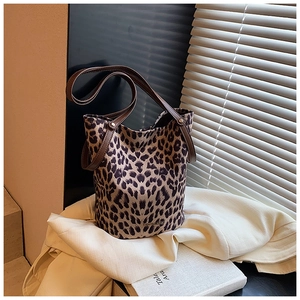 Detailed view of leopard print canvas bucket bag with brown leather straps and metal rivets