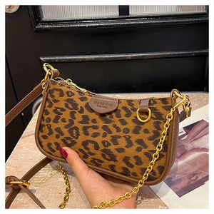Close-up of leopard print baguette bag with brown leather trim and gold chain strap