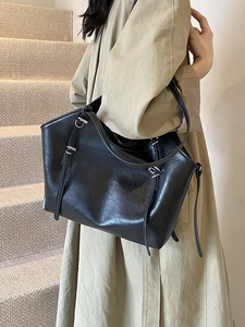 Glossy black faux leather tote bag with silver buckle worn by model on stairs