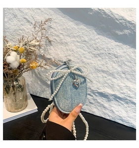 Détail du mini sac bandoulière en denim bleu avec nœud en perles et pendentif cœur argenté
