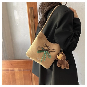 Detail of khaki suede bucket bag with decorative bow and plush dog charm pendant