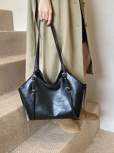 Retro black faux leather tote bag with long straps worn by a model in a trench coat