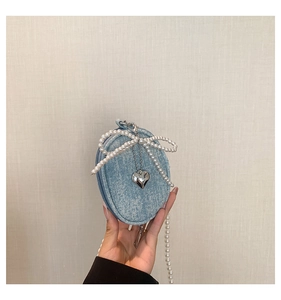Détail d'un mini sac bandoulière en denim avec perles et un pendentif coeur argenté