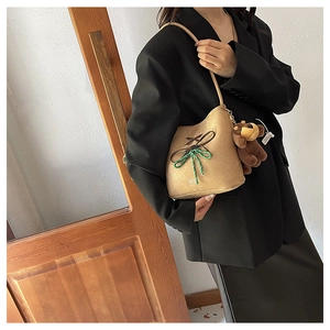Close-up of camel suede bucket bag with woven knot detail and plush bear charm