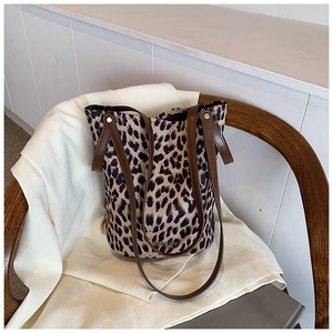Detailed close-up of leopard print canvas bucket bag with brown leather straps and metal rivets