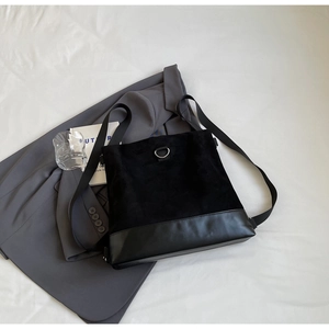 Close-up of black minimalist tote bag with mixed textures and D-ring buckle on a suit