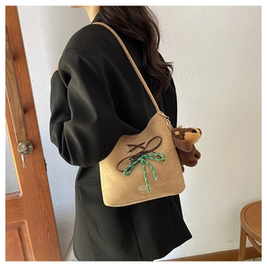 Detail of camel suede bucket bag with decorative bow tie and cute brown teddy bear charm