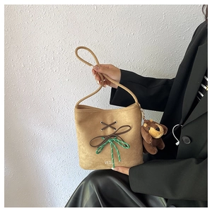 Close-up of brown suede bucket bag featuring cross-lace detail and plush dog charm