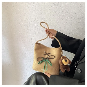 Detail of tan suede shoulder bag featuring green woven knots and a brown dog plush charm