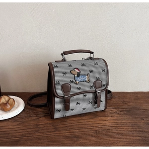 Detail view of houndstooth crossbody bag with cartoon dog patch and brown leather trim