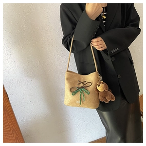 Detail of suede shoulder bag featuring a brown bow knot and a cute plush dog charm