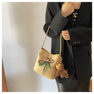 Detail of camel suede bucket bag with decorative bow and cute puppy charm on strap