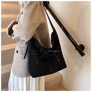 Detail of black suede shoulder bag with contrast stitching and decorative bow detail