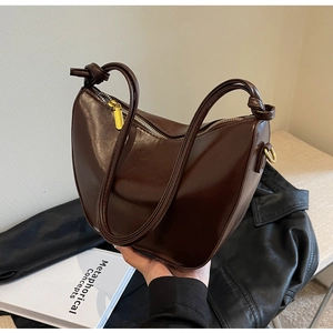 Detail of dark brown leather crescent bag featuring knot straps and gold-tone metal zipper