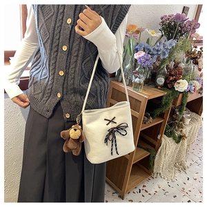 Detail of off-white canvas bucket bag featuring a decorative bow and plush bear charm